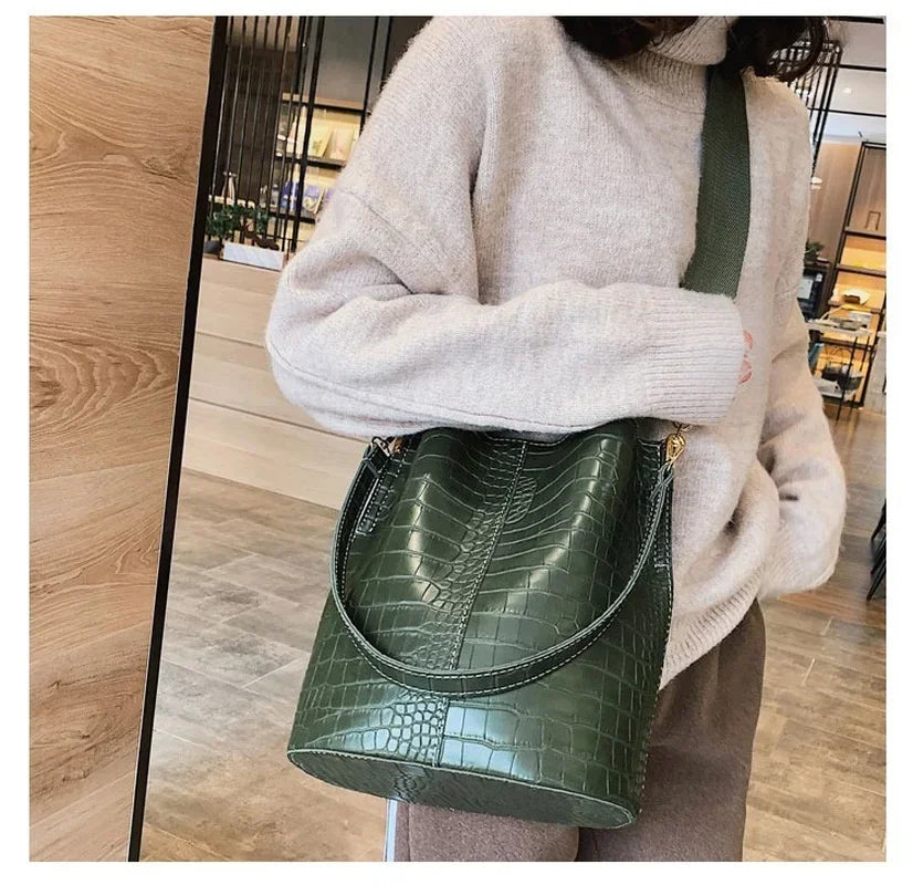 A light beige sweater sleeve holds a dark green alligator pattern leather crossbody bag.