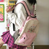 Un sac à dos rose et noir avec un motif de chat est porté par une personne, associé à une jupe à carreaux roses.