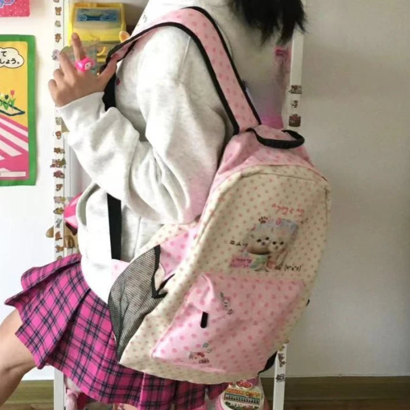 Un sac à dos rose et noir avec un motif de chat est porté par une personne, associé à une jupe à carreaux roses.