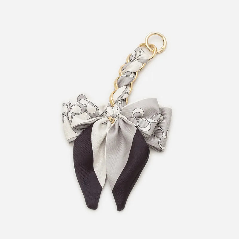 A beige and black adjustable bag strap with a decorative bow and gold clasp.