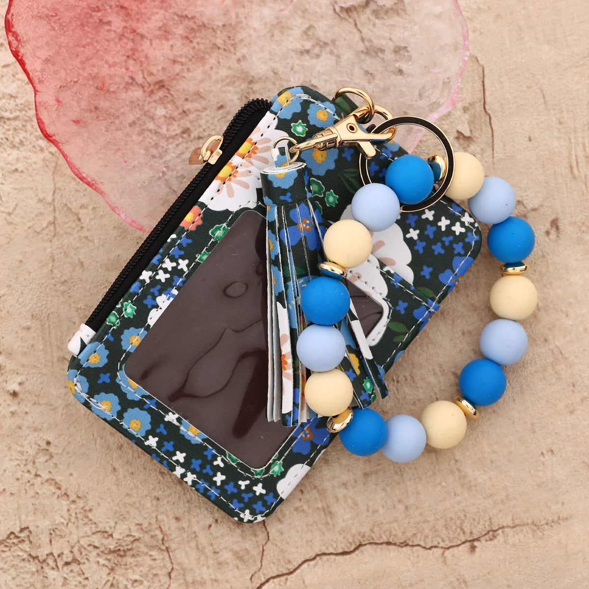 Cartera llavero de cuero PU de silicona floral rosa con cremallera y pulsera de cuentas sobre fondo claro.