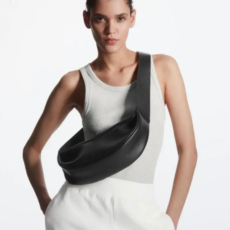 Una modelo vistiendo una camiseta blanca y pantalones claros, sosteniendo un bolso cruz de cuero negro.
