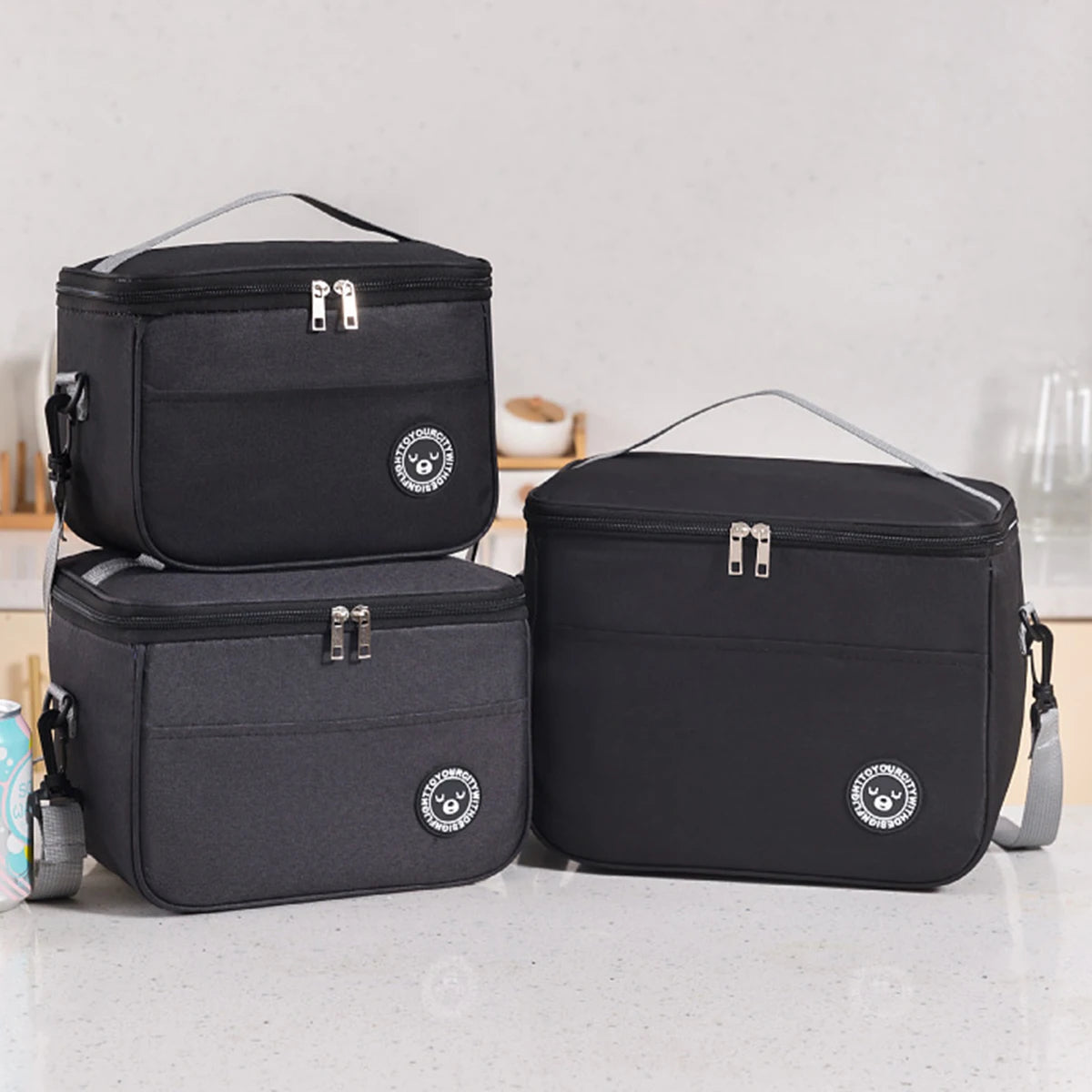 A set of black insulated lunch tote bags with adjustable shoulder straps resting on a white surface.