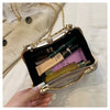 A hand holds a gold glitter crossbody evening clutch bag with a dark interior and a light beige envelope in the background.
