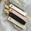 A collection of personalized leather wristlet keychains in various colors and finishes laid on a light fabric background.