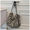 A black and white striped canvas tote bag with black leather handles hanging on a white door frame.