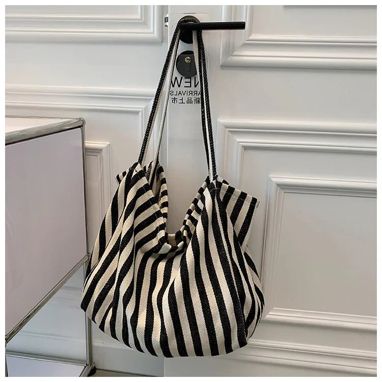 A black and white striped canvas tote bag with black leather handles hanging on a white door frame.