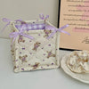A quilted cotton storage basket with a lace flower design and purple ribbon, next to a framed piece of writing.