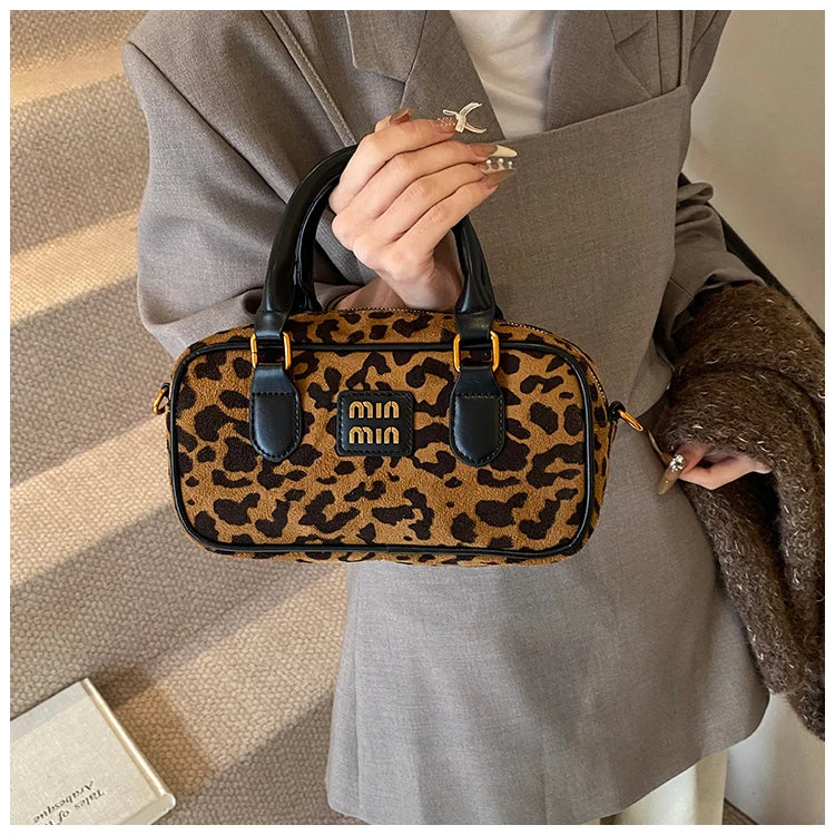 Nahaufnahme einer Leopard-Print-Designer-Hobo-Tasche, getragen von einer Person in einem grauen Blazer.