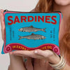 Sac de maquillage bleu sarcelle avec un design de sardines et le texte : Sardines pêchées durablement dans de l'huile d'olive