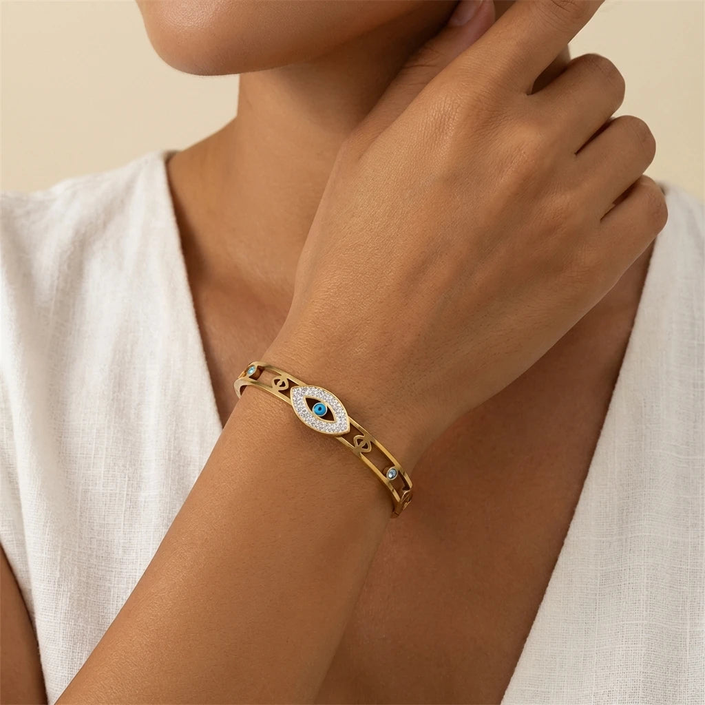 A close-up of a woman's wrist wearing an evil eye crystal cuff bracelet in gold.