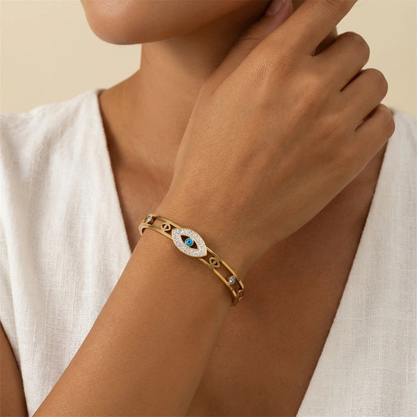A close-up of a woman's wrist wearing an evil eye crystal cuff bracelet in gold.