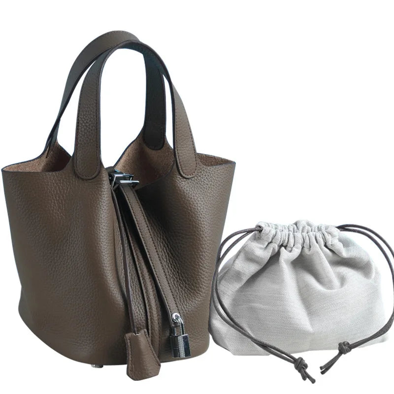 Braune, echte Leder-Bucket-Bag mit Reißverschluss und Schnurverschluss neben ihrer Stofftasche.