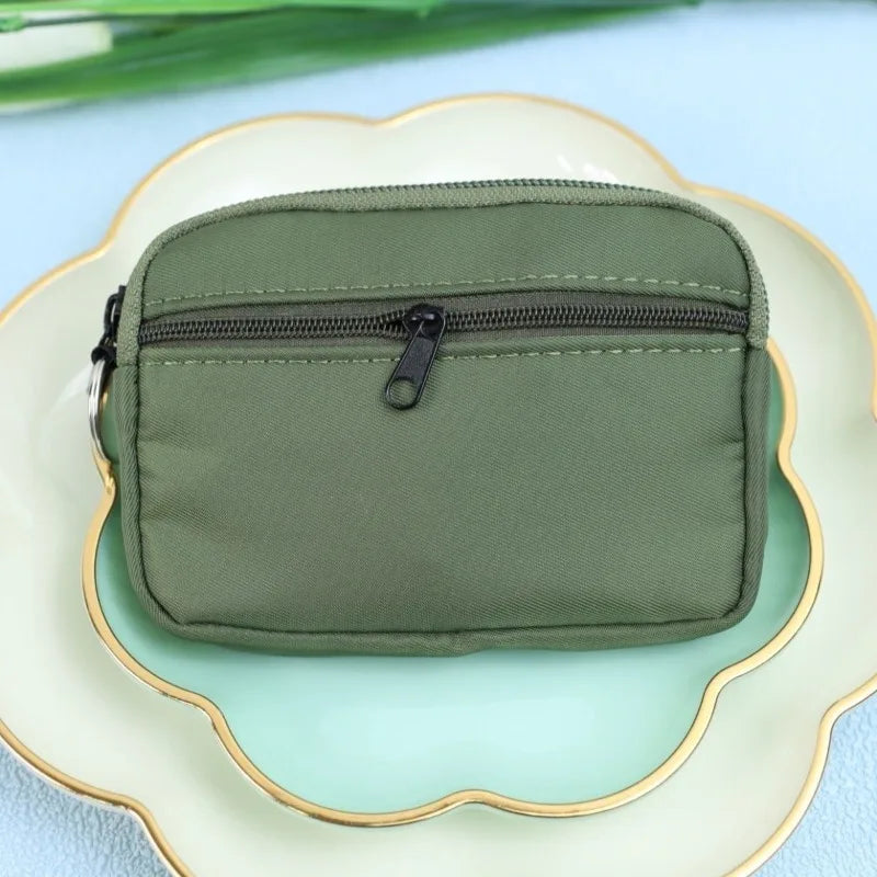 A olive green nylon mini coin purse with a double zipper is placed on a light ceramic plate.