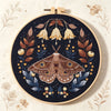 A circular embroidery hoop featuring a detailed butterfly design in brown, gold, and dark blue thread on a black background.