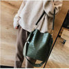 A close-up of a dark green alligator pattern leather crossbody bag carried by a person wearing a beige sweater and brown pant