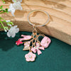 Porte-clés doré avec nœuds de fleurs roses en forme de cœur et un petit charme de sac rose sur une surface de velours vert.