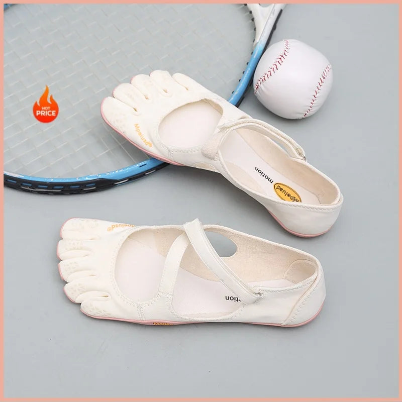 A pair of white women's barefoot five-toe shoes with an adjustable strap and a leather ball are displayed on a light gray sur