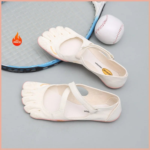 A pair of white women's barefoot five-toe shoes with an adjustable strap and a leather ball are displayed on a light gray sur
