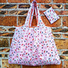 A pink and white patterned foldable reusable shopping bag resting on a brick wall.
