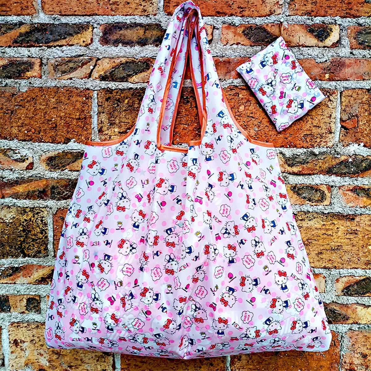 A pink and white patterned foldable reusable shopping bag resting on a brick wall.