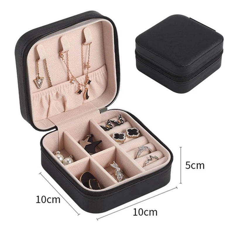 A black compact leather jewelry travel box open to show various necklaces and earrings.