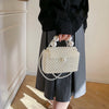 A person holds a white pearl beaded clutch bag with a silver chain strap against a light background.