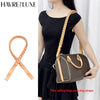 A woman models a brown leather shoulder bag with a matching strap against a white background.