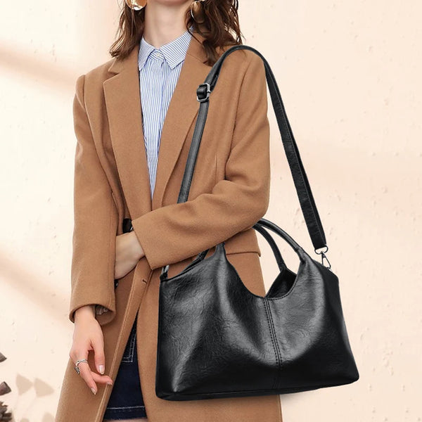 A woman wearing a tan blazer and blue striped shirt holds a black leather crossbody shoulder bag.