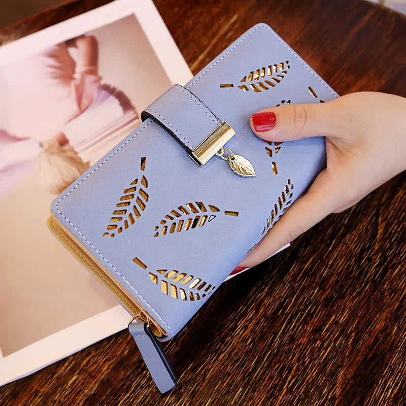 Cartera de cuero sintético azul claro con detalles en hoja de oro, sostenida por una mano sobre una superficie de madera junt