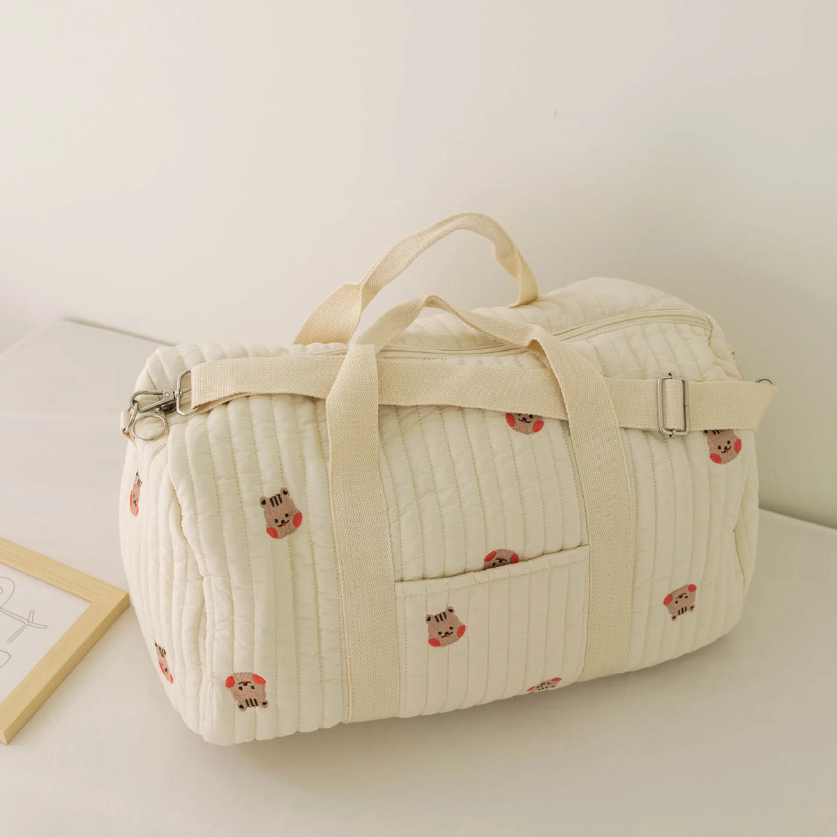 A cream quilted diaper bag tote with a light beige strap and small bear embroidery.