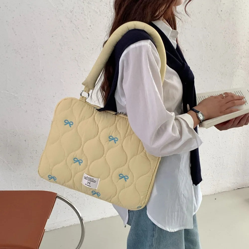 Una mujer sostiene un bolso de computadora acolchado amarillo claro con detalles de lazo azul.
