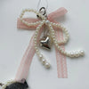 A pink lace bow made of pearls with a silver heart charm attached, used as a keychain.