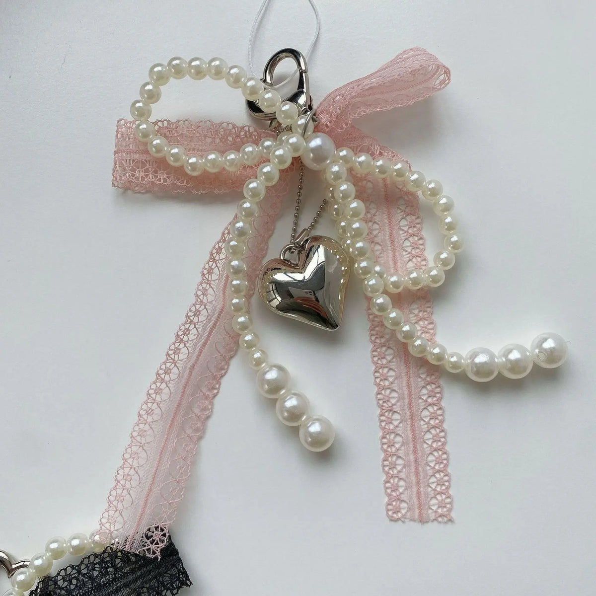 A pink lace bow made of pearls with a silver heart charm attached, used as a keychain.