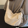 A light beige canvas crossbody shoulder bag is shown against a neutral gray hoodie.