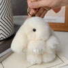 A fluffy white rabbit plush toy with a black nose is being held by a hand, shown against a light background.