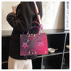 A woman holds a pink and purple ladies' shoulder tote bag with a black jacket in a modern interior setting.
