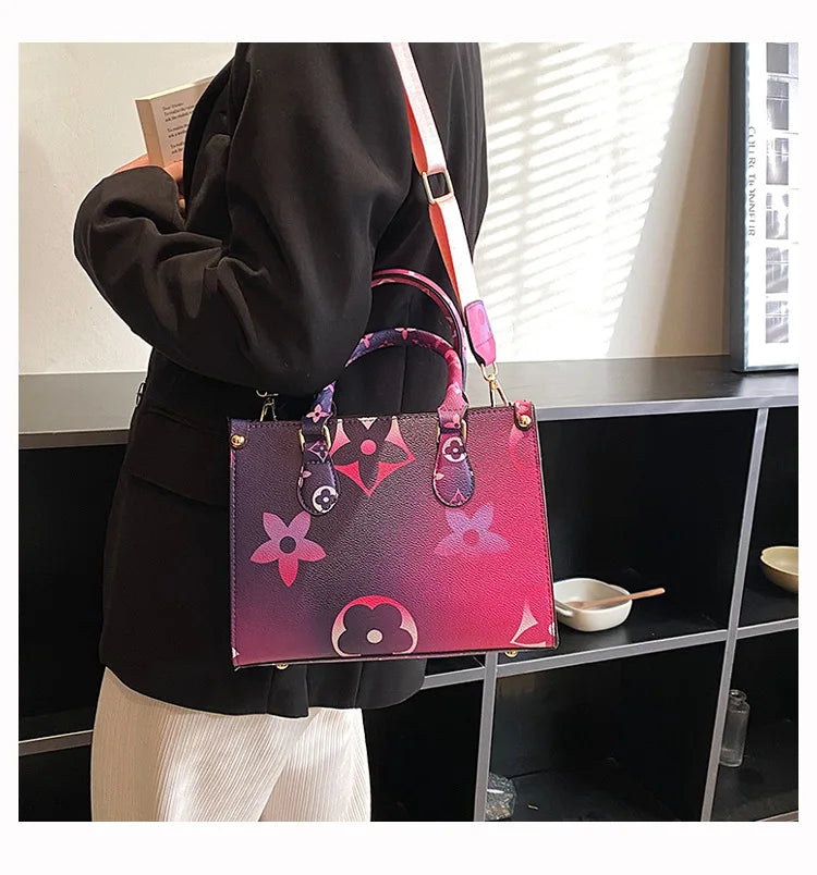 A woman holds a pink and purple ladies' shoulder tote bag with a black jacket in a modern interior setting.