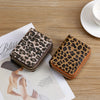 A brown leopard print PU leather compact wallet resting on a wooden table next to a magazine.