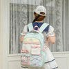 A woman wearing a white dress and a baseball cap is shown from the back carrying a light blue candy color campus backpack.