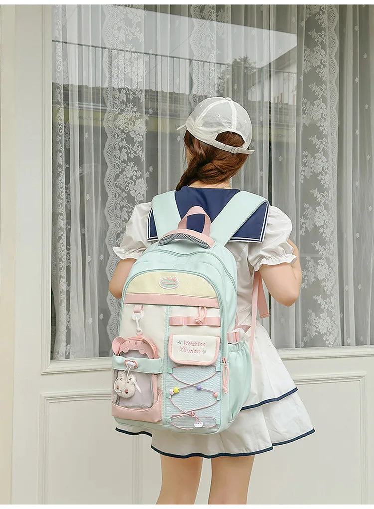 A woman wearing a white dress and a baseball cap is shown from the back carrying a light blue candy color campus backpack.