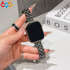 A hand is holding a black Apple Watch with a sparkling metal strap featuring crystal fishscales.