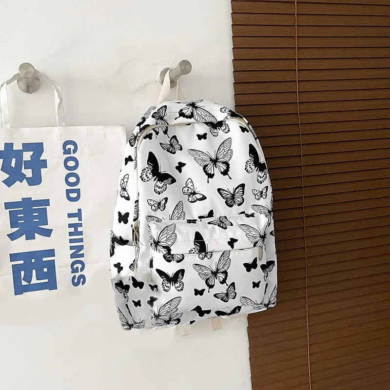 White backpack featuring a black butterfly pattern, hanging against a light background.