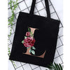 Black canvas tote bag featuring a large gold letter L with an accompanying floral print.