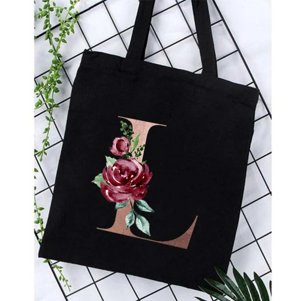 Black canvas tote bag featuring a large gold letter L with an accompanying floral print.