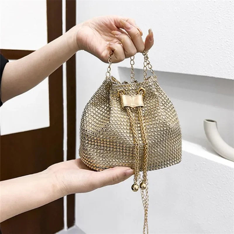 Una mano sostiene un bolso cruz de cordón brillante con pedrería tono dorado.