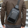 A man wearing a brown leather jacket holds a black geometric pattern crossbody bag.