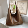 A brown PU leather slouchy hobo shoulder bag hanging on a hanger in front of a window with tulips.