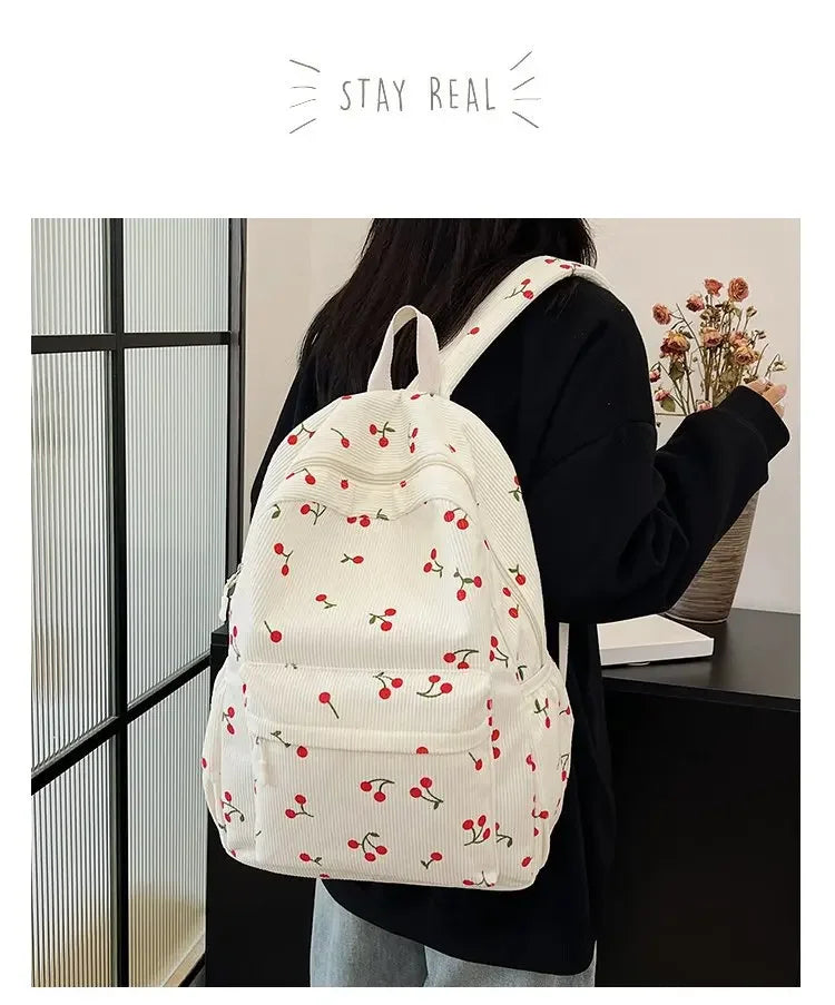 A woman is wearing a white corduroy fashion backpack with red berries and green leaves against a dark background.