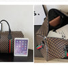 A brown plaid women's travel duffle bag is shown next to a tablet.